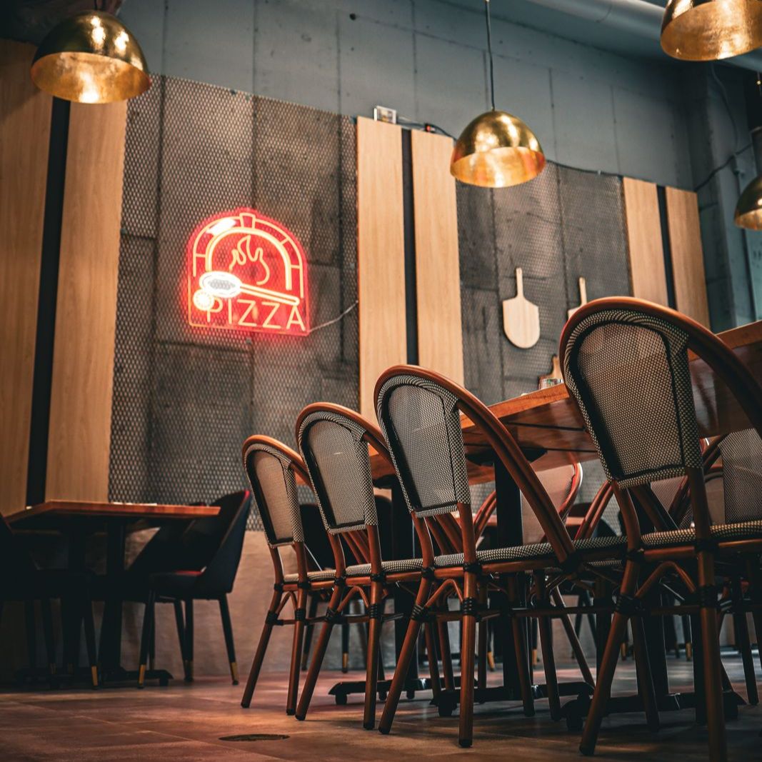 Dining corner at Pēpe Kitchen with neon pizza sign, wood-slat panels, and brass pendants