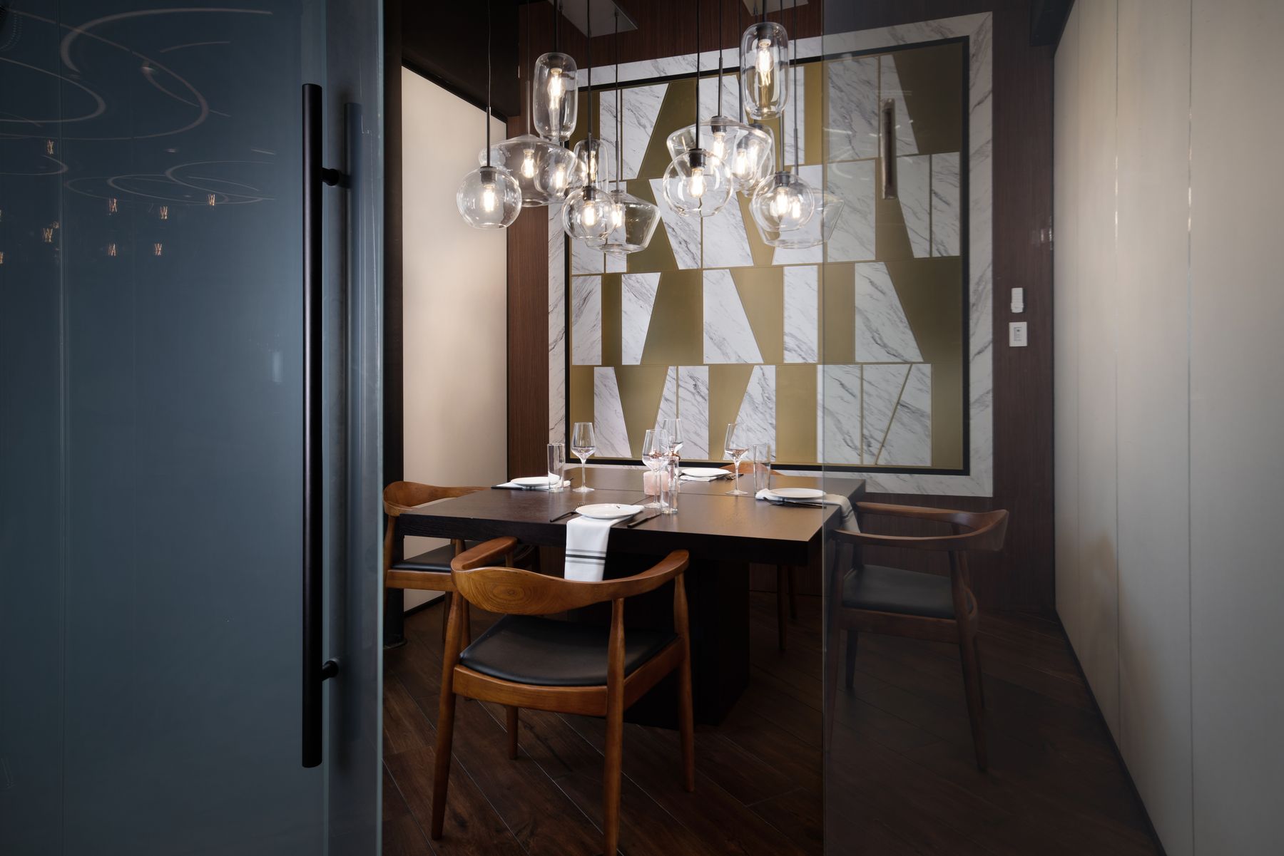 The glass-enclosed private dining room at SALT: marble-and-brass feature wall under a cluster of glass pendants